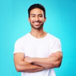 Smile, confident and portrait of Asian man arms crossed with casual fashion isolated in a studio bl
